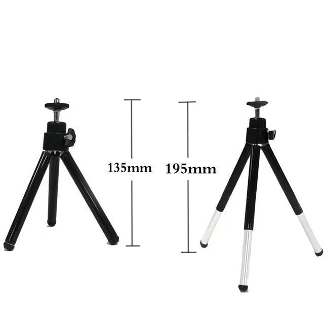 Black mini camera tripod with extended legs and a separate U-shaped universal phone clip on a table.