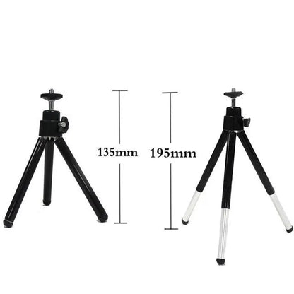 Black mini camera tripod with extended legs and a separate U-shaped universal phone clip on a table.