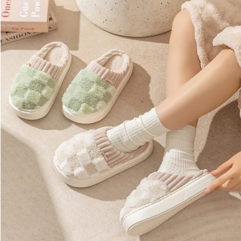 Plaid pattern women's plush slippers with coral velvet upper and textured PVC sole on a wooden floor.