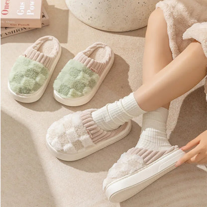 Plaid pattern women's plush slippers with coral velvet upper and textured PVC sole on a wooden floor.