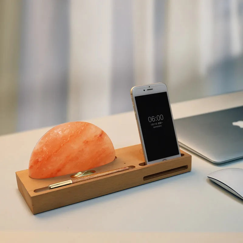Natural crystal salt lamp with wooden base on a table, wirelessly charging a smartphone.