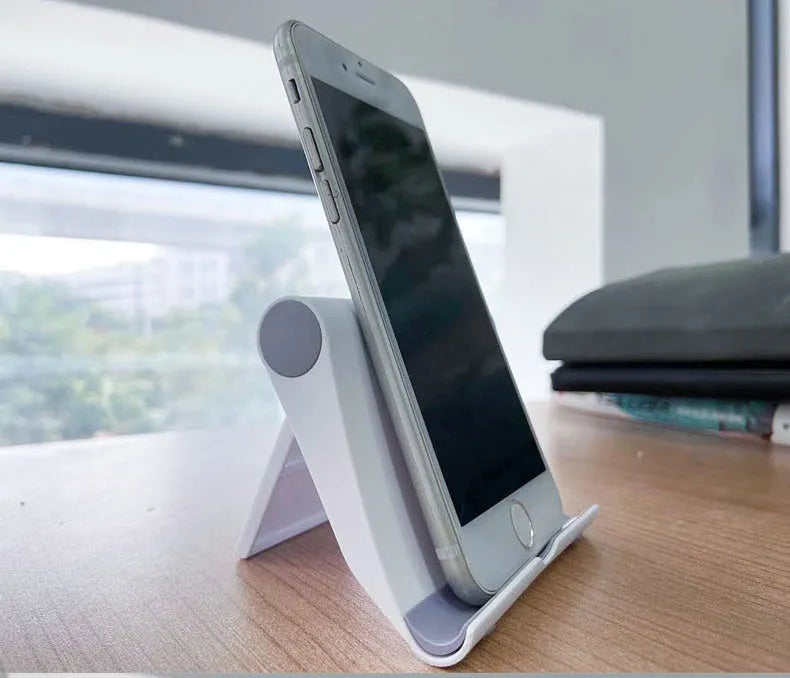 Black PE folding mobile phone stand holding a smartphone at an angle on a desktop.