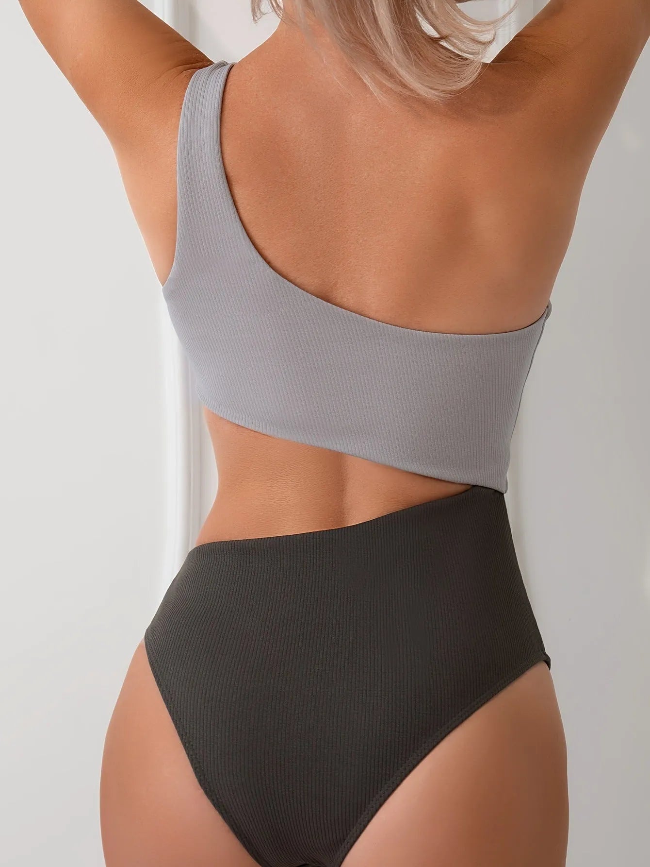 Light grey one-shoulder one-piece swimsuit on a mannequin, showing the single strap and solid colour design.