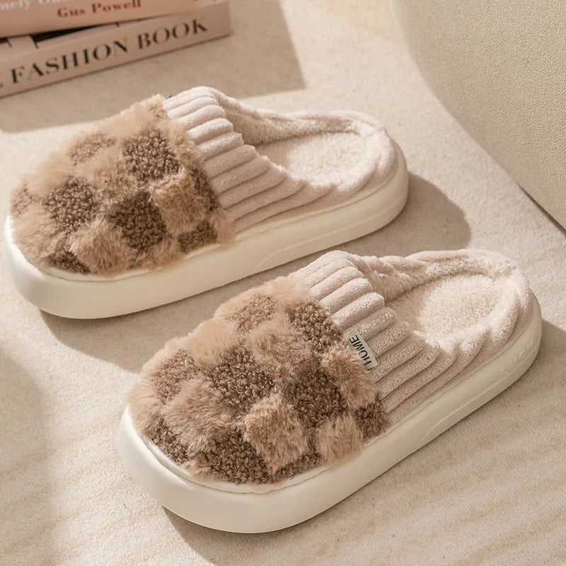 Plaid pattern women's plush slippers with coral velvet upper and textured PVC sole on a wooden floor.