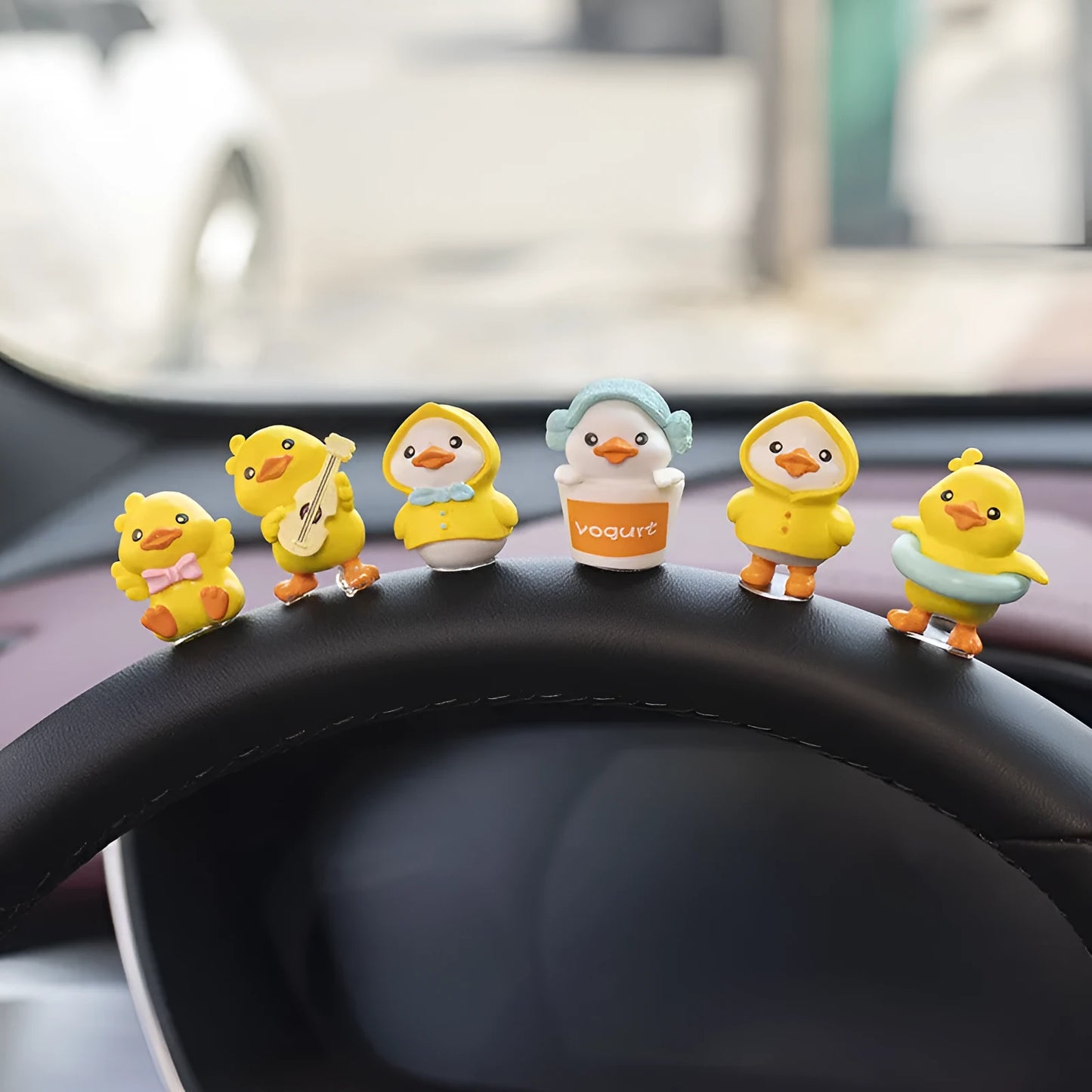 Set of six small yellow PVC duckling car decorations and one cartoon sign on a car dashboard.