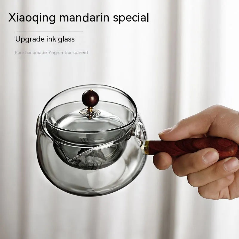 Transparent borosilicate glass rotary teapot with wooden handle and built-in infuser on a wooden surface