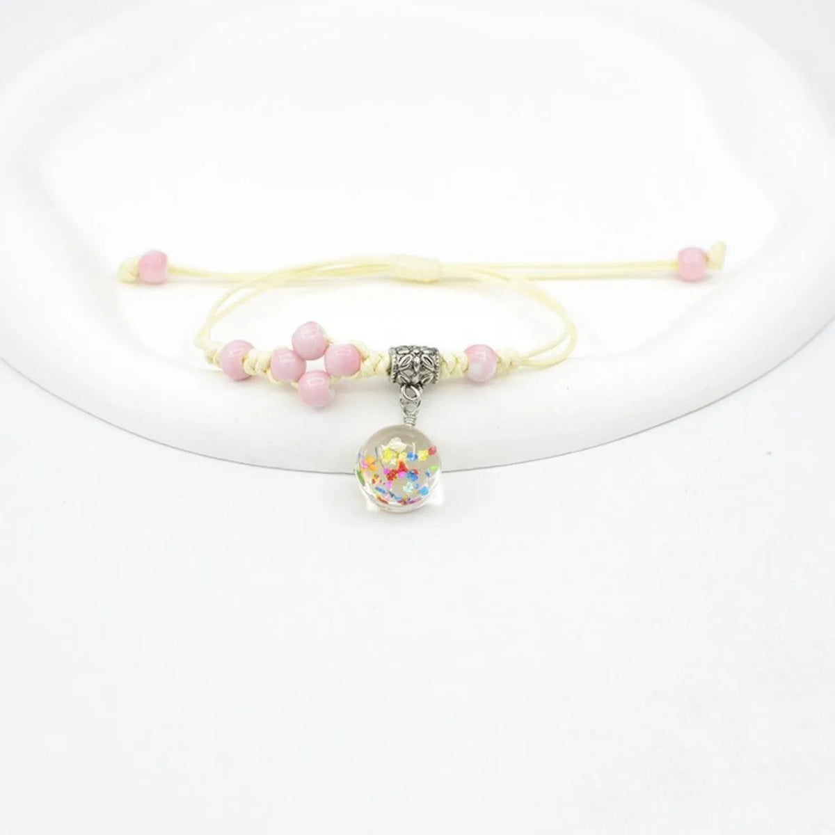 Close-up of a hand-woven bracelet with a large 1.4cm glass bead containing colourful dried flowers.