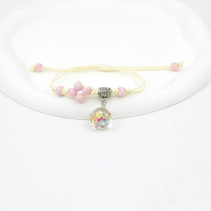 Close-up of a hand-woven bracelet with a large 1.4cm glass bead containing colourful dried flowers.