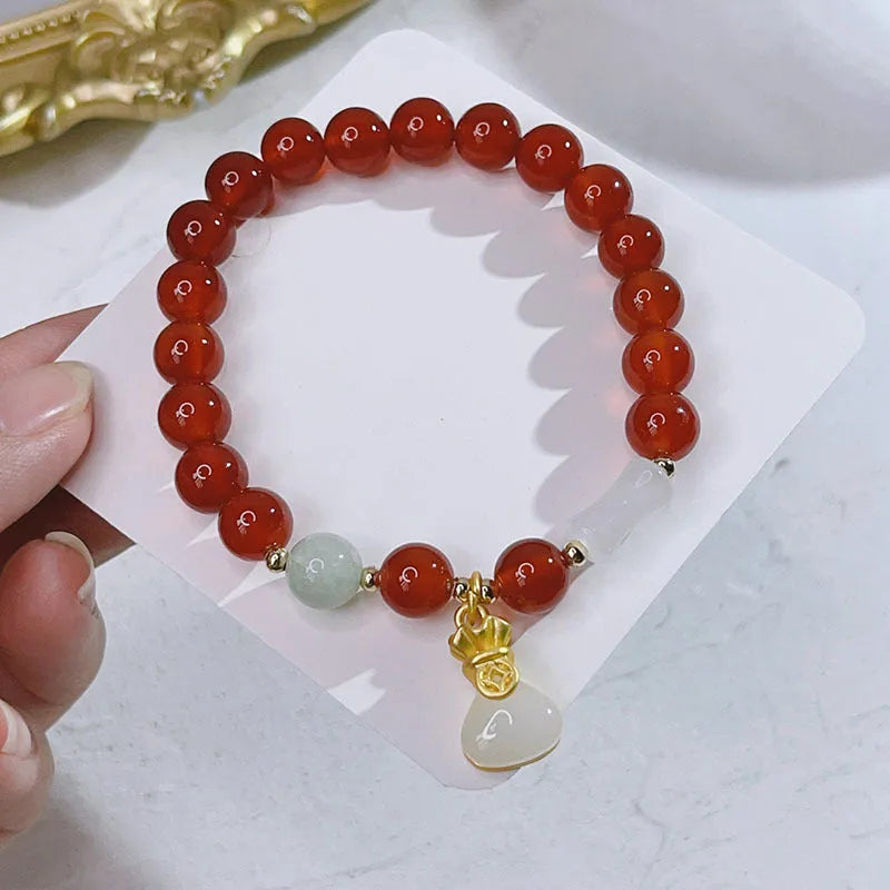 Close-up of a red agate bracelet with a dragon charm and Lucky Bag symbol on a wrist.