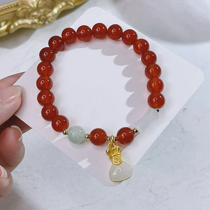 Close-up of a red agate bracelet with a dragon charm and Lucky Bag symbol on a wrist.