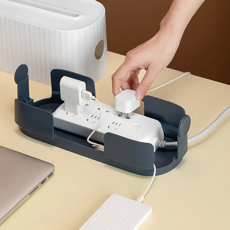 Blue desktop cable storage box with a white lid, showing cable ports on the base and a mobile phone sitting in its slot on top.