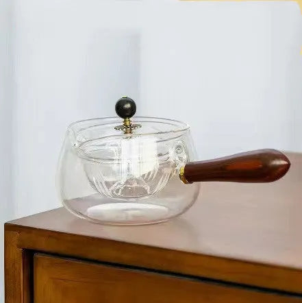 Transparent borosilicate glass rotary teapot with wooden handle and built-in infuser on a wooden surface
