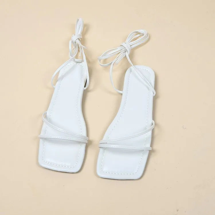Women's white ankle-ring flat sandals with bandage cloth strap and front lace-up on a rubber sole.