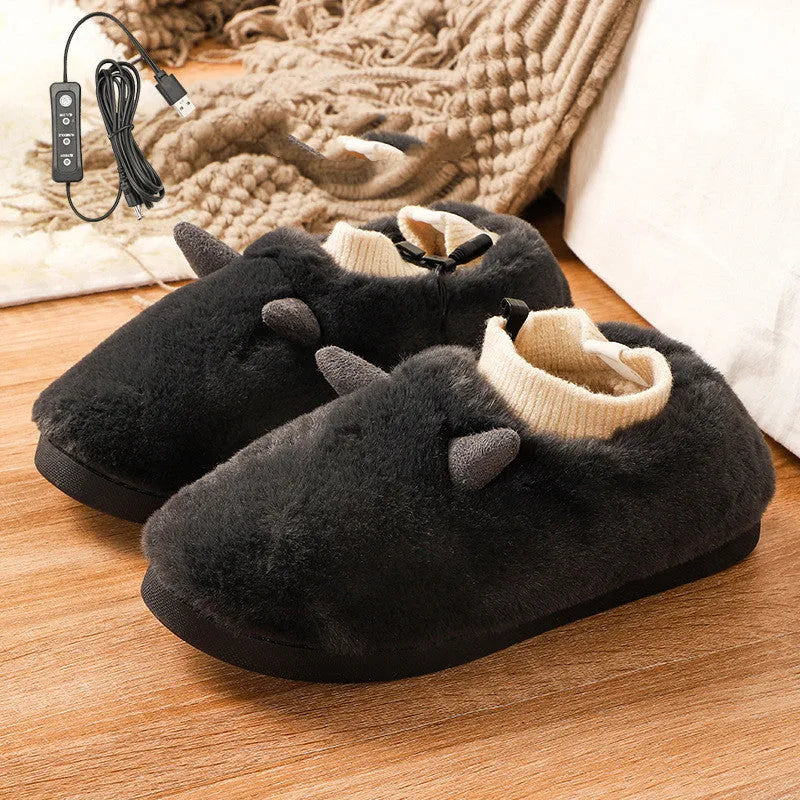 USB heating slippers in black plugged into a laptop, showing the cable and soft velvet upper.
