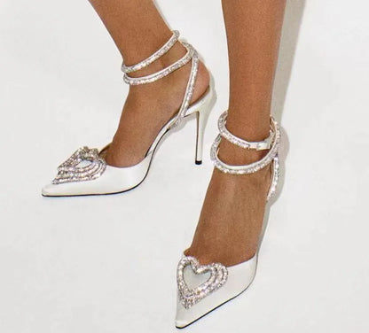 Women's pink satin sandals with heart-shaped rhinestone toe holders and adjustable cross straps on a white background.