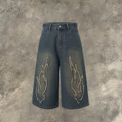 Men's black cropped denim shorts with a red and yellow flame embroidery patch on the leg.