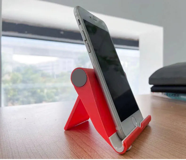 Black PE folding mobile phone stand holding a smartphone at an angle on a desktop.