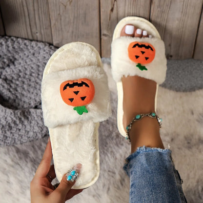 Yellow Halloween pumpkin plush open-toe slippers with synthetic fur and a textured PVC sole, shown on a wooden floor.
