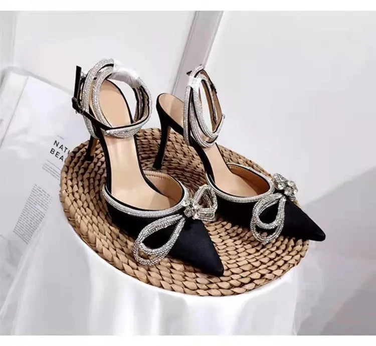 Women's black stiletto heel sandals with silk bandage ankle strap and buckle fastening on a pointed toe.