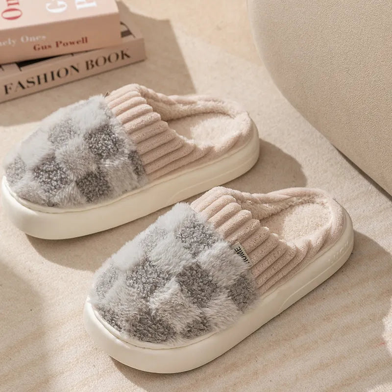 Plaid pattern women's plush slippers with coral velvet upper and textured PVC sole on a wooden floor.