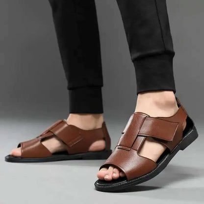 Men's brown leather Roman sandals with an open toe and rubber sole on a wooden surface.
