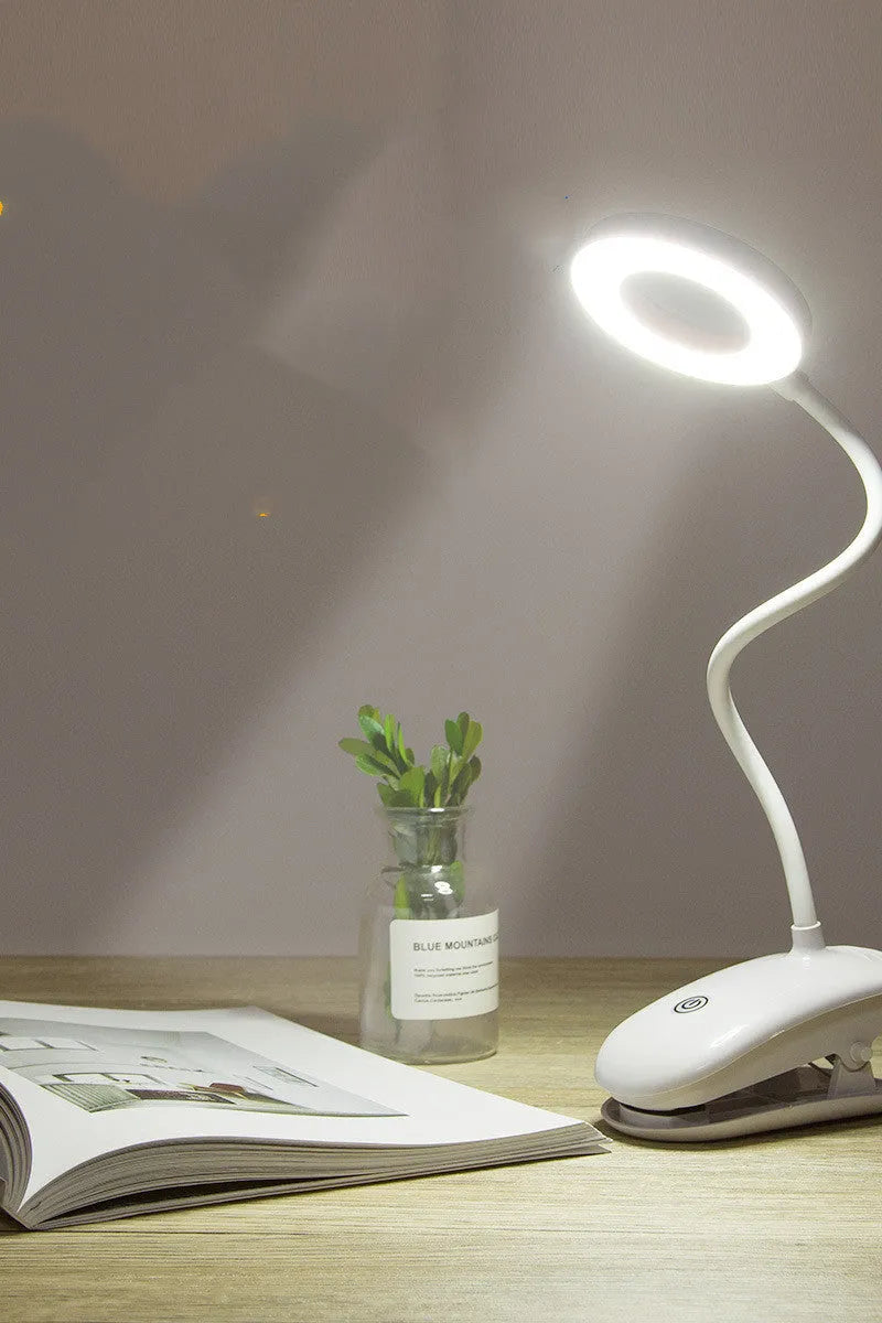 A modern white clip-on rechargeable desk lamp with a touch-sensitive switch and a plastic shade.