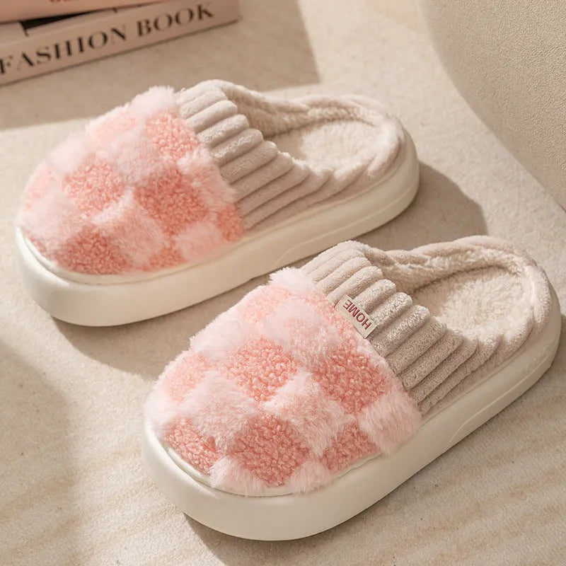 Plaid pattern women's plush slippers with coral velvet upper and textured PVC sole on a wooden floor.