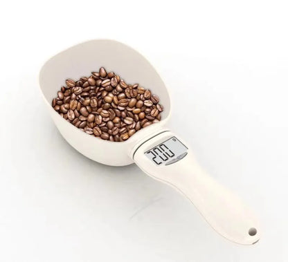 White electronic pet feeding weighing spoon with digital display and removable metal shovel head on a table.