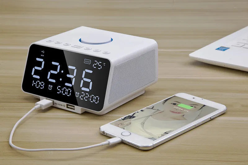Black and white wireless alarm clock Bluetooth speaker with remote control on a table.