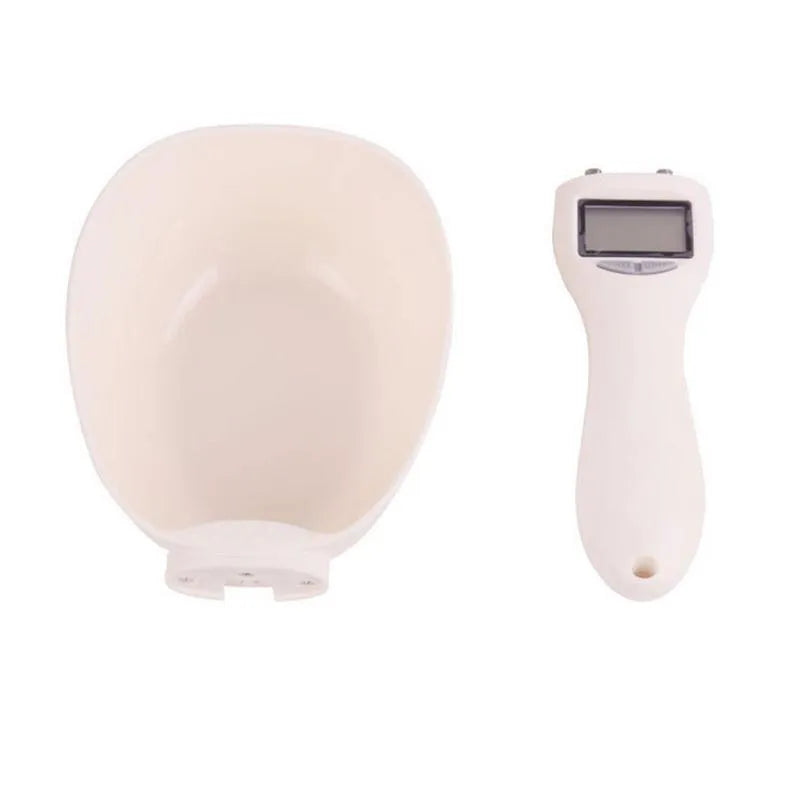 White electronic pet feeding weighing spoon with digital display and removable metal shovel head on a table.