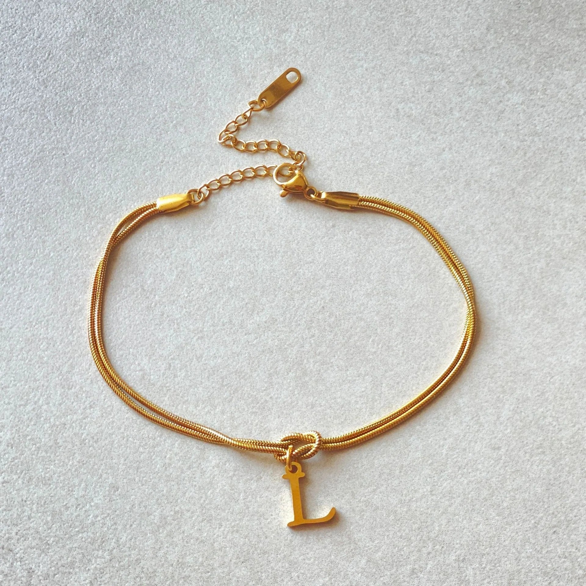 Elegant letter charm bracelets for women in gold and silver tones, featuring a delicate snake chain design and personalised letter charms.