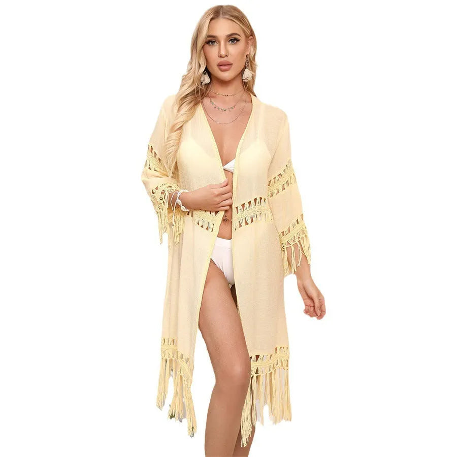 Yellow hand-crocheted acrylic beach cover-up cardigan with tassels, laid flat on a sandy background.