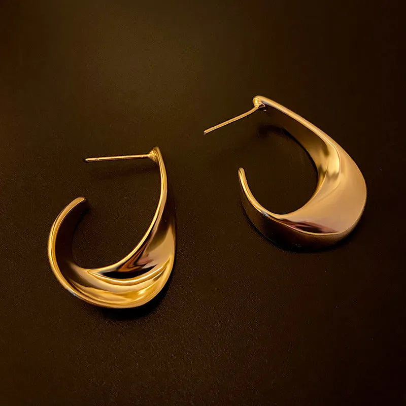 A pair of gold twisted geometric metal earrings with a round detail on a white background.