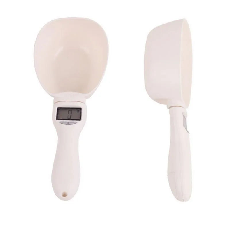 White electronic pet feeding weighing spoon with digital display and removable metal shovel head on a table.