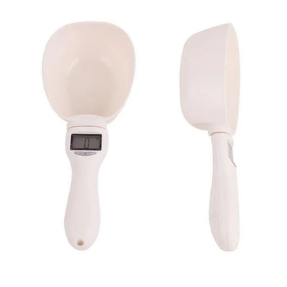 White electronic pet feeding weighing spoon with digital display and removable metal shovel head on a table.
