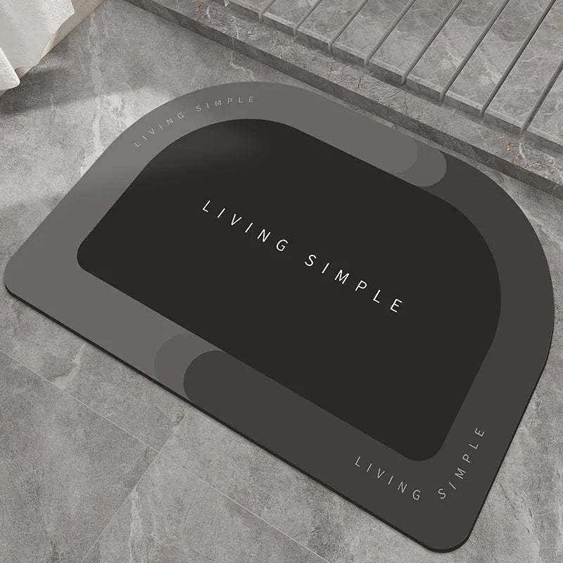 Oval grey bath mat with non-slip rubber bottom on a tiled floor, showing absorbent fabric surface