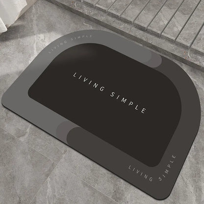 Oval grey bath mat with non-slip rubber bottom on a tiled floor, showing absorbent fabric surface