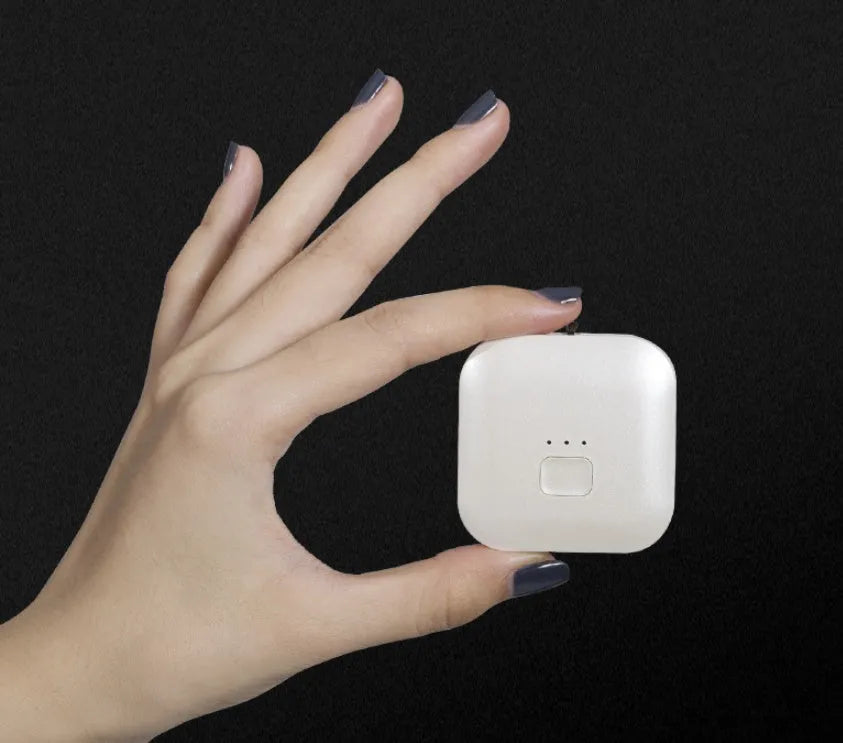 Small pink wearable air purifier pendant on a necklace, showing USB charging port and single button.