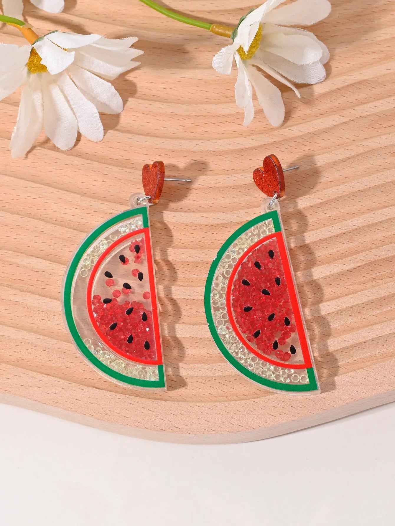 A pair of colourful acrylic earrings shaped like a strawberry and a cherry on a woman's ear.