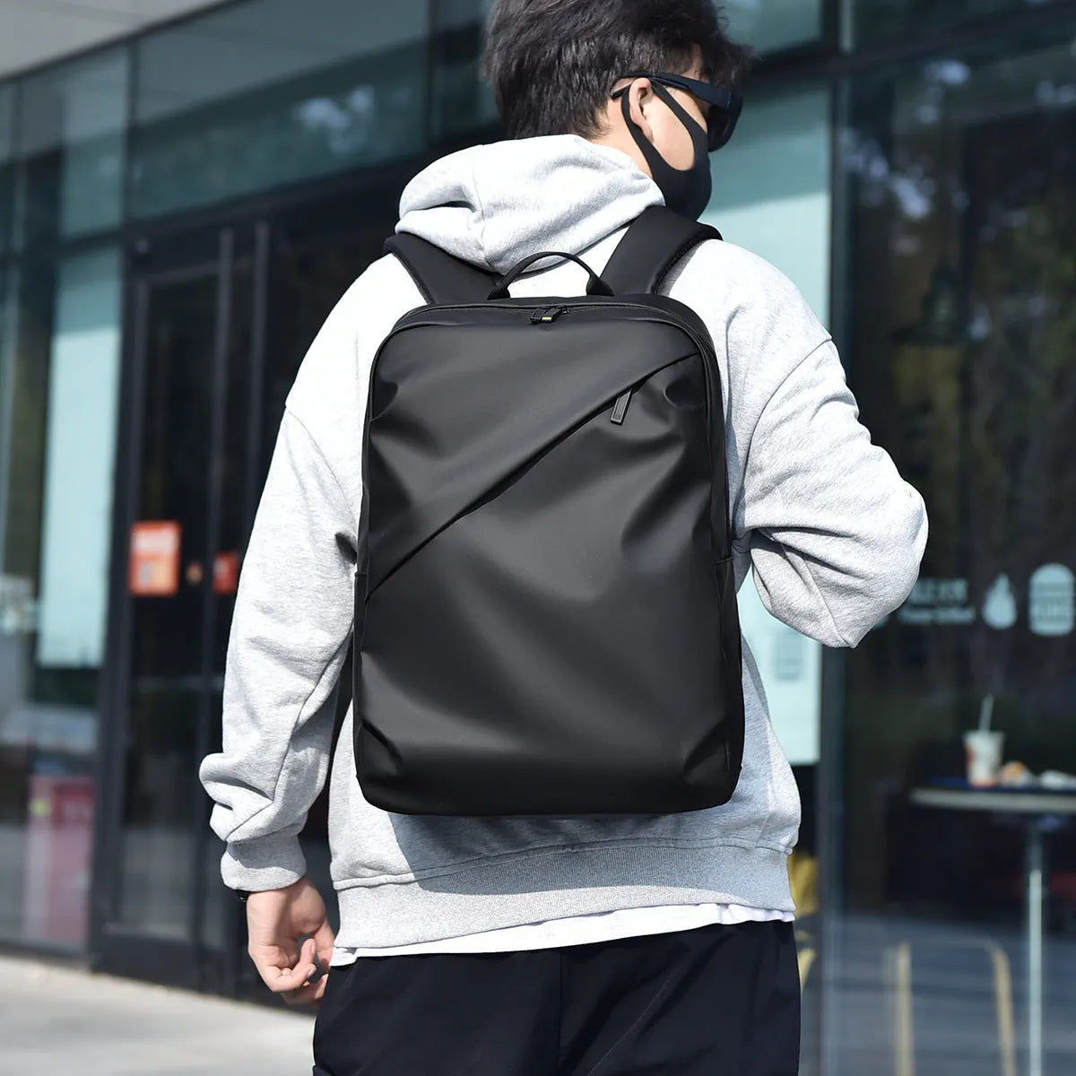 Large black waterproof PU leather laptop backpack with sewing thread details on a simple design.