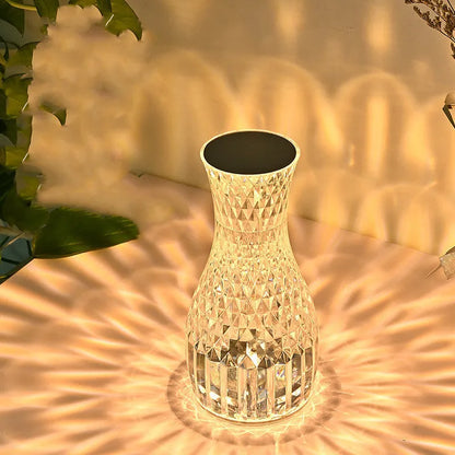 Vase-shaped crystal table lamp with remote control on a bedside table, showing diamond-like glow and USB charging port.