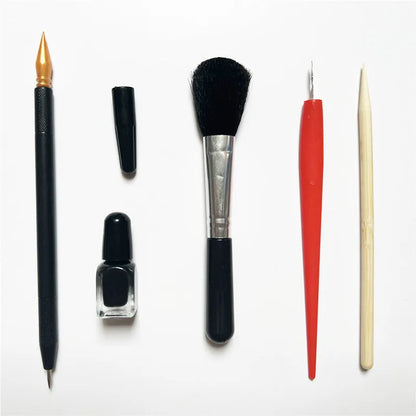 Diamond painting repair tool set with metal scraper pen, bottle of adhesive liquid, soft brush, and bamboo stick on a craft table