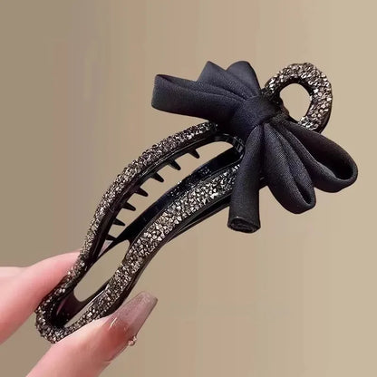A black crystal bow on a clear 11.5cm long acrylic banana hair clip with bobby pin back.