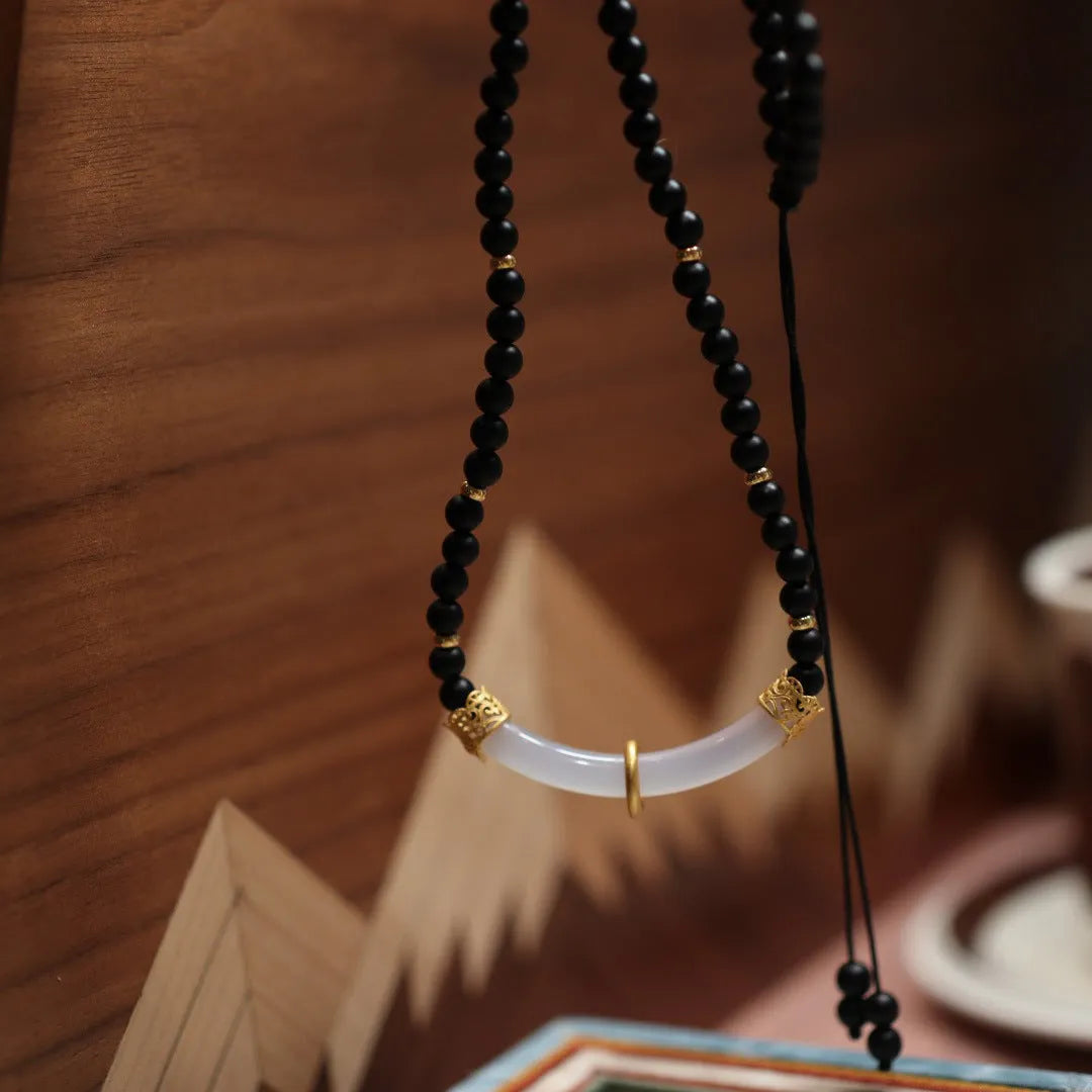 Close-up of a U-shaped necklace with frosted black agate, white chalcedony, and a 925 silver pendant on a beaded chain.