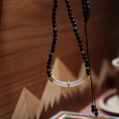 Close-up of a U-shaped necklace with frosted black agate, white chalcedony, and a 925 silver pendant on a beaded chain.