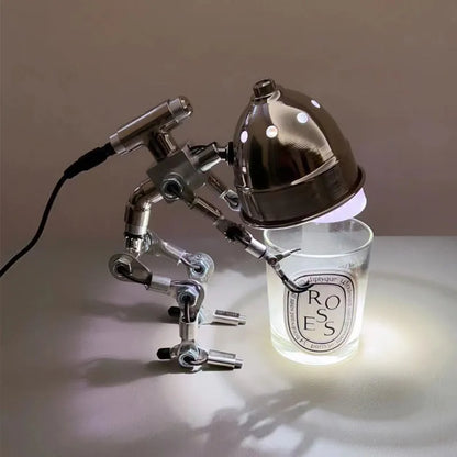 Silver copper robot-shaped decorative desk lamp with custom graphic option on a wooden shelf.
