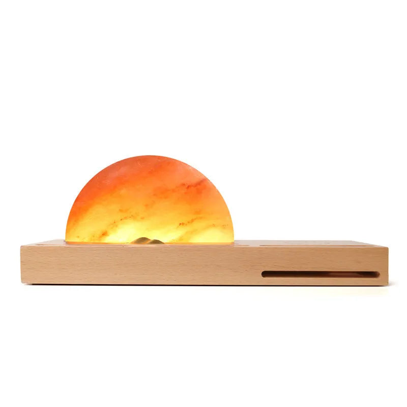 Natural crystal salt lamp with wooden base on a table, wirelessly charging a smartphone.