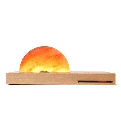Natural crystal salt lamp with wooden base on a table, wirelessly charging a smartphone.