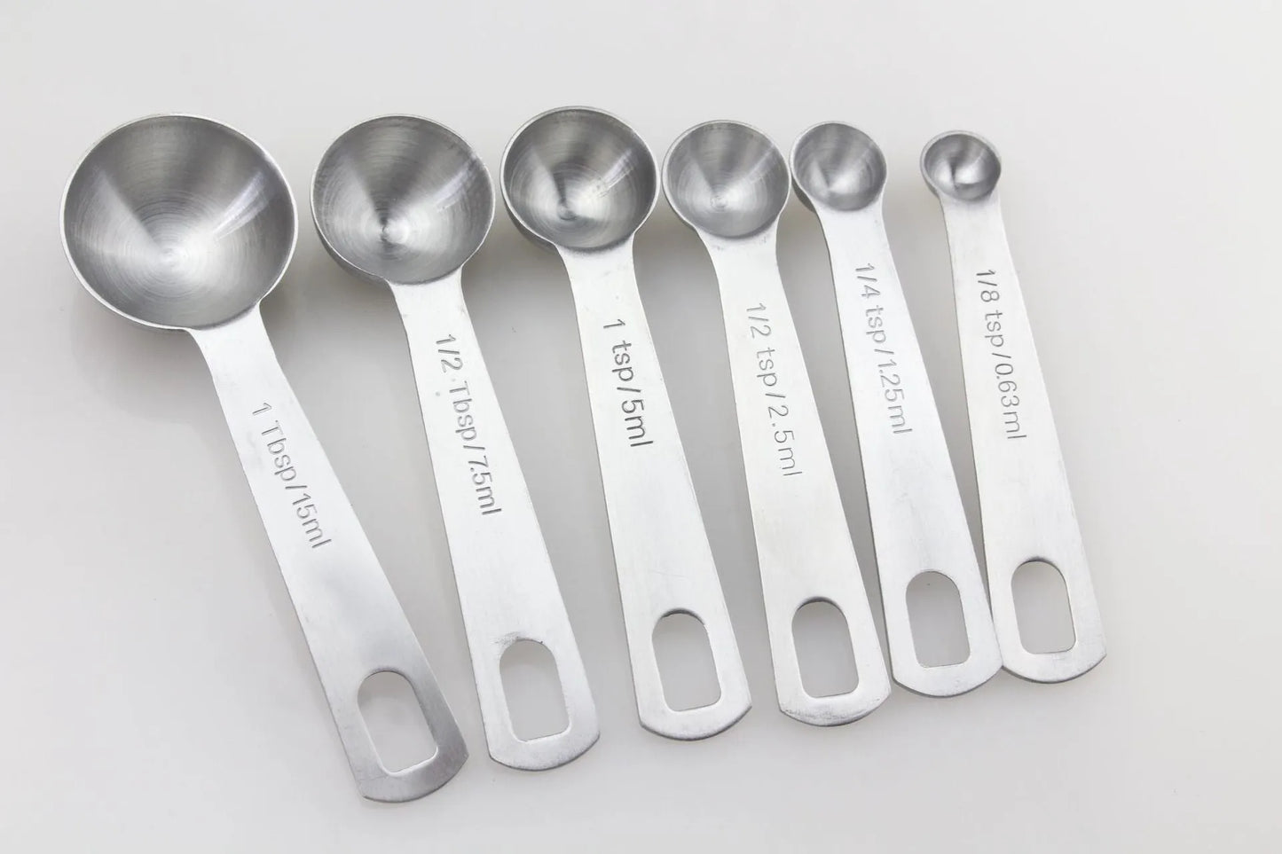 Set of six stainless steel measuring spoons connected by a silver D-ring, showing engraved measurement markings