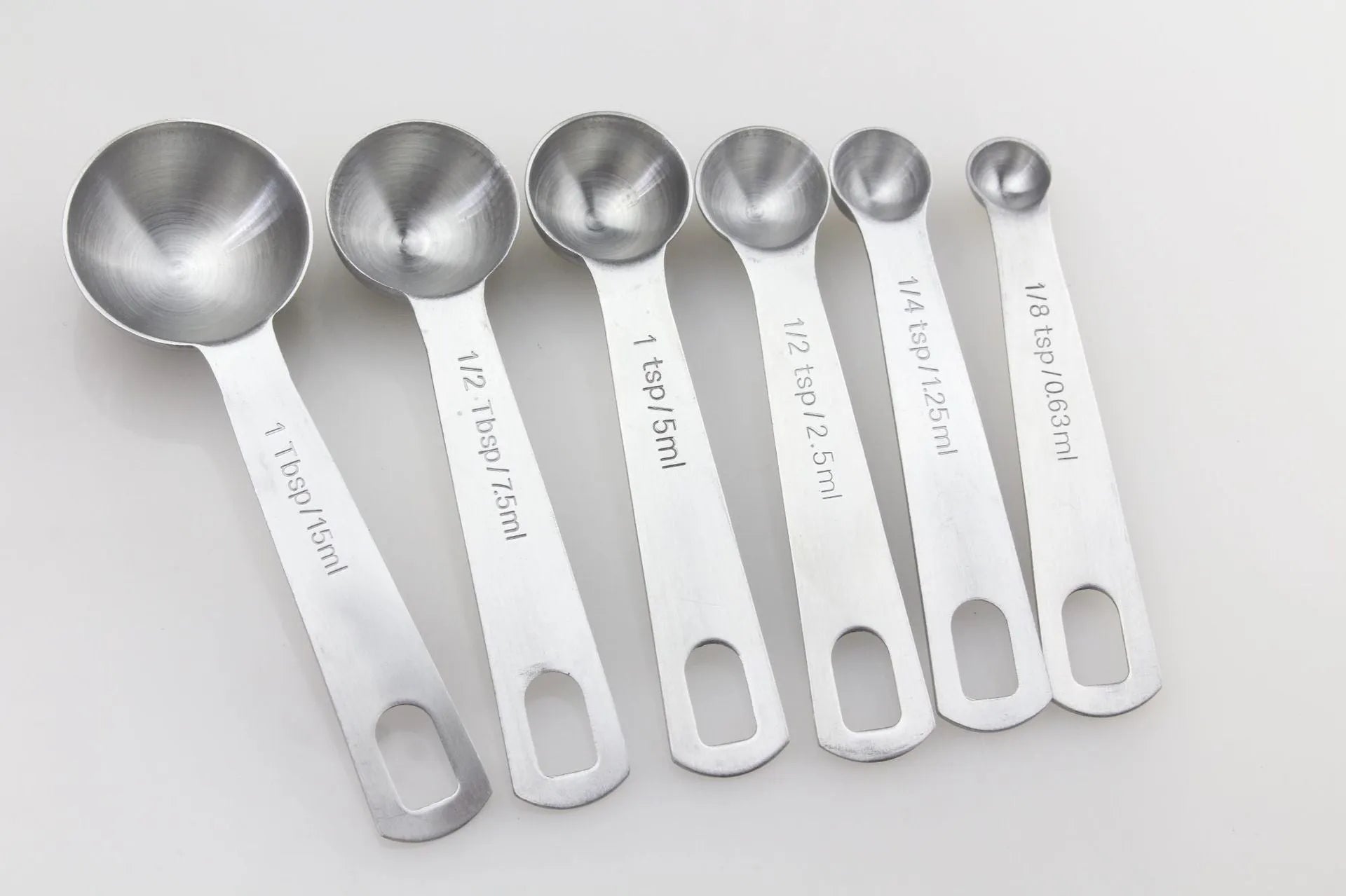 Set of six stainless steel measuring spoons connected by a silver D-ring, showing engraved measurement markings
